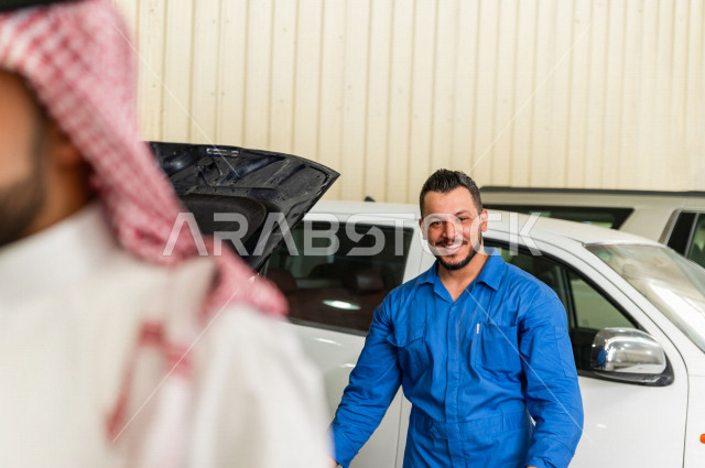 رجل  عربي سعودي يقف مع المهندس الميكانيكي داخل ورشة السيارات  ، بايماءات وجه و يدين مختلفة  ، خدمات اصلاح و صيانة السيارات ، مهندس ميكانيكي ، ورشة صيانة 