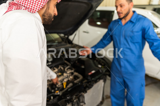 رجل عربي سعودي  داخل ورشة السيارات  ، بصحبة مهندس ميكانيكي يقوم باصلاح سيارته ، استخدام ادوات للصيانة ، اصلاح يدوي ، خدمات اصلاح و صيانة السيارات ، مهندس ميكانيكي ، ورشة صيانة 