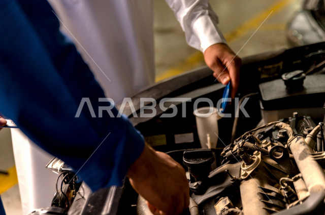 رجل عربي سعودي  داخل ورشة السيارات  ، بصحبة مهندس ميكانيكي يقوم باصلاح سيارته ، استخدام ادوات للصيانة ، اصلاح يدوي ، خدمات اصلاح و صيانة السيارات ، مهندس ميكانيكي ، ورشة صيانة 