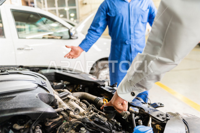 رجل عربي سعودي  داخل ورشة السيارات  ، بصحبة مهندس ميكانيكي يقوم باصلاح سيارته ، استخدام ادوات للصيانة ، اصلاح يدوي ، خدمات اصلاح و صيانة السيارات ، مهندس ميكانيكي ، ورشة صيانة 