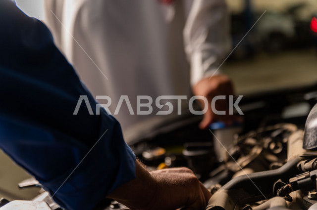 رجل عربي سعودي  داخل ورشة السيارات  ، بصحبة مهندس ميكانيكي يقوم باصلاح سيارته ، استخدام ادوات للصيانة ، اصلاح يدوي ، خدمات اصلاح و صيانة السيارات ، مهندس ميكانيكي ، ورشة صيانة 