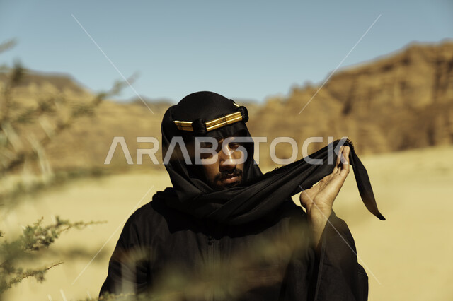 التكوينات والتشكيلات الصخرية في محافظة العلا بالمملكة العربية السعودية, صورة مقربة لشاب عربي خليجي سعودي يرتدي العقال الذهبي ينظر إلى شيء ما في إحدى المعالم الأثرية المشهورة, يوم بدينا 1727م, ذكرى تأسيس الدولة السعودية الأولى في 22 فبراير