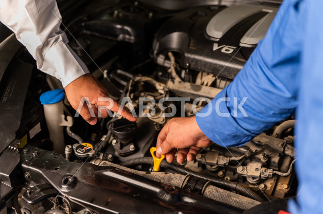 رجل عربي سعودي  داخل ورشة السيارات  ، بصحبة مهندس ميكانيكي يقوم باصلاح سيارته ، استخدام ادوات للصيانة ، اصلاح يدوي ، خدمات اصلاح و صيانة السيارات ، مهندس ميكانيكي ، ورشة صيانة 