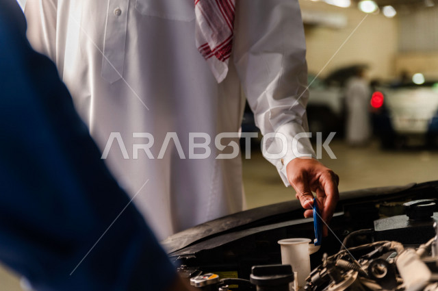 رجل عربي سعودي  داخل ورشة السيارات  ، بصحبة مهندس ميكانيكي يقوم باصلاح سيارته ، استخدام ادوات للصيانة ، اصلاح يدوي ، خدمات اصلاح و صيانة السيارات ، مهندس ميكانيكي ، ورشة صيانة 