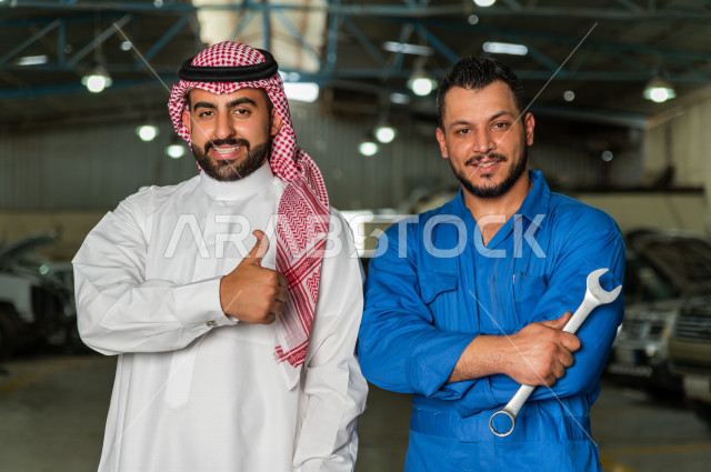 رجل  عربي سعودي يقف مع المهندس الميكانيكي داخل ورشة السيارات  ، بايماءات وجه و يدين مختلفة  ، خدمات اصلاح و صيانة السيارات ، مهندس ميكانيكي ، ورشة صيانة 