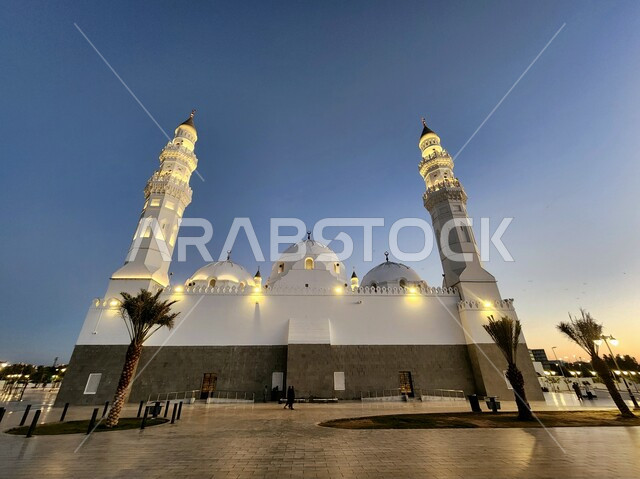 دعوة المسلمين لآداء الصلاة، الساحة الخارجية لمسجد قباء في المدينة المنورة وقت الغروب، معالم و أماكن دينية مقدسة في المملكة العربية السعودية، العبادة والتقرب إلى الله، المآذن و القبب المضيئة، الفن الهندسي المعماري والديكورات الاسلامية على الطراز الحديث