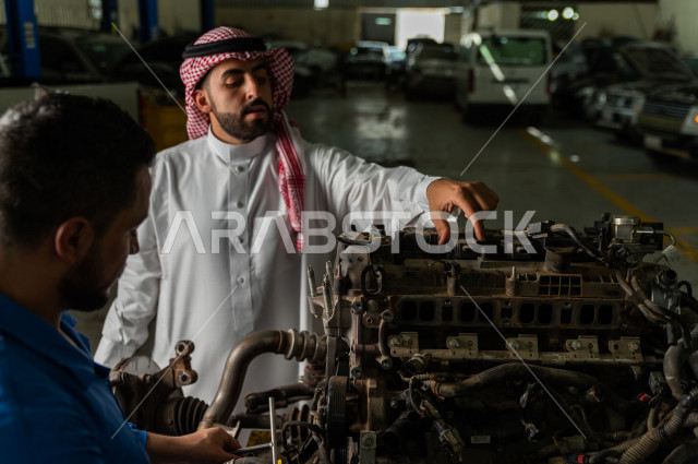 رجل عربي سعودي  داخل ورشة السيارات  ، بصحبة مهندس ميكانيكي يقوم باصلاح سيارته ، استخدام ادوات للصيانة ، اصلاح يدوي ، خدمات اصلاح و صيانة السيارات ، مهندس ميكانيكي ، ورشة صيانة 