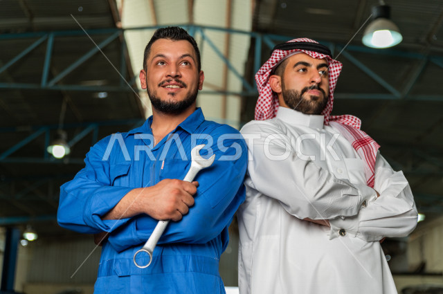 رجل  عربي سعودي يقف مع المهندس الميكانيكي داخل ورشة السيارات  ، بايماءات وجه و يدين مختلفة  ، خدمات اصلاح و صيانة السيارات ، مهندس ميكانيكي ، ورشة صيانة 