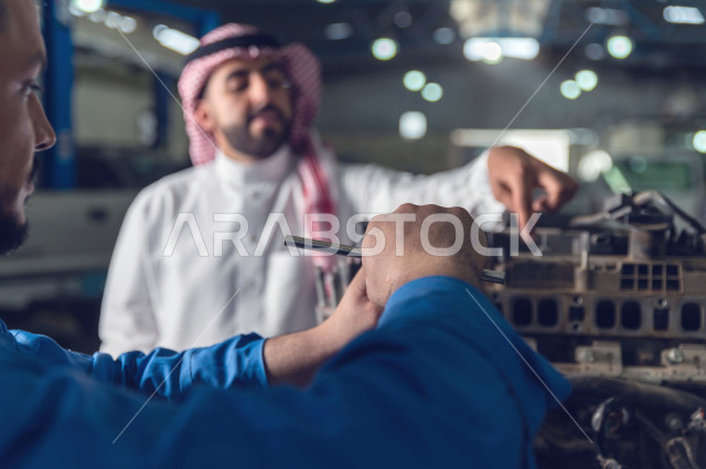 رجل عربي سعودي  داخل ورشة السيارات  ، بصحبة مهندس ميكانيكي يقوم باصلاح سيارته ، استخدام ادوات للصيانة ، اصلاح يدوي ، خدمات اصلاح و صيانة السيارات ، مهندس ميكانيكي ، ورشة صيانة 