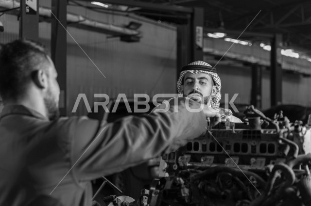 رجل عربي سعودي  داخل ورشة السيارات  ، بصحبة مهندس ميكانيكي يقوم باصلاح سيارته ، استخدام ادوات للصيانة ، اصلاح يدوي ، خدمات اصلاح و صيانة السيارات ، مهندس ميكانيكي ، ورشة صيانة 
