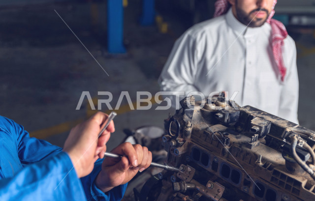 A Saudi Arabian man inside the car workshop, accompanied by a mechanical engineer, is repairing his car, using tools for maintenance, manual repair, car repair and maintenance services, a mechanical engineer, a maintenance workshop