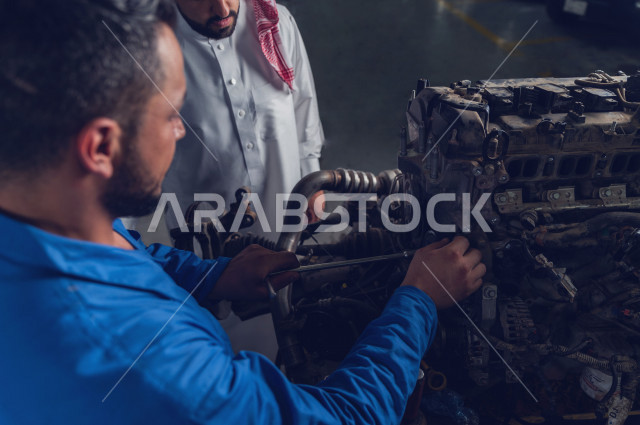  رجل عربي سعودي  داخل ورشة السيارات  ، بصحبة مهندس ميكانيكي يقوم باصلاح سيارته ، استخدام ادوات للصيانة ، اصلاح يدوي ، خدمات اصلاح و صيانة السيارات ، مهندس ميكانيكي ، ورشة صيانة 