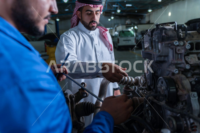 رجل عربي سعودي  داخل ورشة السيارات  ، بصحبة مهندس ميكانيكي يقوم باصلاح سيارته ، استخدام ادوات للصيانة ، اصلاح يدوي ، خدمات اصلاح و صيانة السيارات ، مهندس ميكانيكي ، ورشة صيانة 