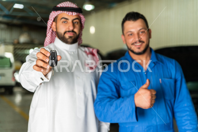 رجل  عربي سعودي يقف مع المهندس الميكانيكي داخل ورشة السيارات  ، تسليم مفاتيح السيارة للعامل  ، خدمات اصلاح و صيانة السيارات ، مهندس ميكانيكي ، ورشة صيانة 