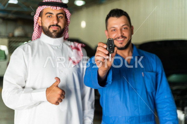 رجل  عربي سعودي يقف مع المهندس الميكانيكي داخل ورشة السيارات  ، تسليم مفاتيح السيارة للعامل  ، خدمات اصلاح و صيانة السيارات ، مهندس ميكانيكي ، ورشة صيانة 