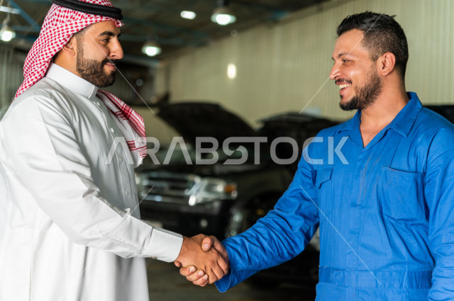 رجل  عربي سعودي يقف مع المهندس الميكانيكي داخل ورشة السيارات  ، تسليم مفاتيح السيارة للعامل  ، خدمات اصلاح و صيانة السيارات ، مهندس ميكانيكي ، ورشة صيانة 