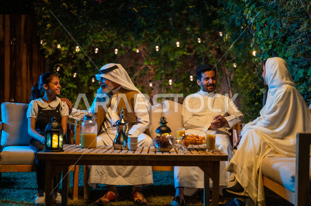 تبادل الأحاديث والتسامر بين الأفراد، أسرة عربية خليجية سعودية تقضي أوقات ممتعة في جلسة خارجية في احدى الشاليهات، أجواء عائلية سعيدة في شهر رمضان المبارك، فوانيس معدنية مضيئة وديكورات وزينة المناسبات والأعياد الاسلامية