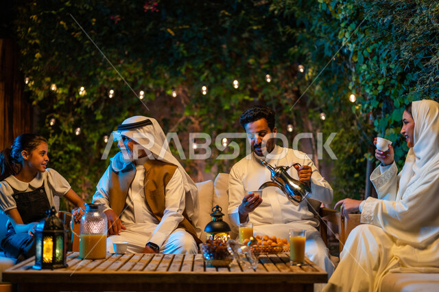 شرب القهوة الساخنة بعد الإفطار، تبادل الأحاديث والتسامر بين الأفراد، أسرة عربية خليجية سعودية تقضي أوقات ممتعة في جلسة خارجية في احدى الشاليهات، أجواء عائلية سعيدة في شهر رمضان المبارك، فوانيس معدنية مضيئة وديكورات وزينة المناسبات والأعياد الاسلامية