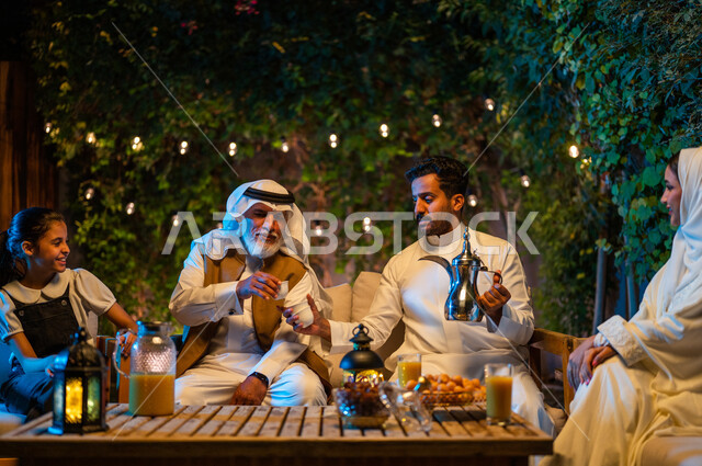 شرب القهوة الساخنة بعد الإفطار، تبادل الأحاديث والتسامر بين الأفراد، أسرة عربية خليجية سعودية تقضي أوقات ممتعة في جلسة خارجية في احدى الشاليهات، أجواء عائلية سعيدة في شهر رمضان المبارك، فوانيس معدنية مضيئة وديكورات وزينة المناسبات والأعياد الاسلامية