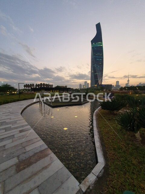 الفن المعماري لبرج التجارية المطل على حديقة الشهيد في منطقة الكويت الثقافية الوطنية الجديدة، المناطق والأماكن العائلية للتنزه والمتعة، المروج الخضراء والأشجار والبيئة الطبيعية وقت الغروب، المسطحات المائية والبحيرات في المنتزهات والحدائق العامة في دولة الكويت