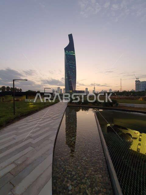 الفن المعماري لبرج التجارية المطل على حديقة الشهيد في منطقة الكويت الثقافية الوطنية الجديدة، المناطق والأماكن العائلية للتنزه والمتعة، المروج الخضراء والأشجار والبيئة الطبيعية وقت الغروب، المسطحات المائية والبحيرات في المنتزهات والحدائق العامة في دولة الكويت