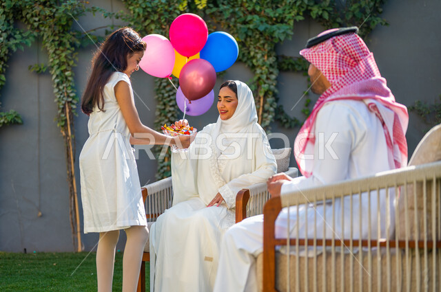 أعياد ومناسبات إسلامية سعيدة, فرحة و بهجة الأطفال في العيد السعيد، فتاة عربية خليجية سعودية ترتدي فستان أبيض تقوم بتقديم قطع السكاكر, عادات العيد في المجتمع السعودي الخليجي, الاحتفال في الهواء الطلق في إحدى الشاليهات والمنتجعات السياحية