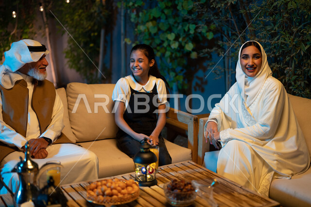 تقوية وتعزيز الروابط الأسرية، تبادل الأحاديث والتسامر بين الأفراد بإيماءات السرور، أسرة عربية خليجية سعودية تقضي أوقات ممتعة في جلسة خارجية في احدى الشاليهات، أجواء عائلية سعيدة في شهر رمضان المبارك، فانوس معدني مضيء زينة المناسبات والأعياد الاسلامية
