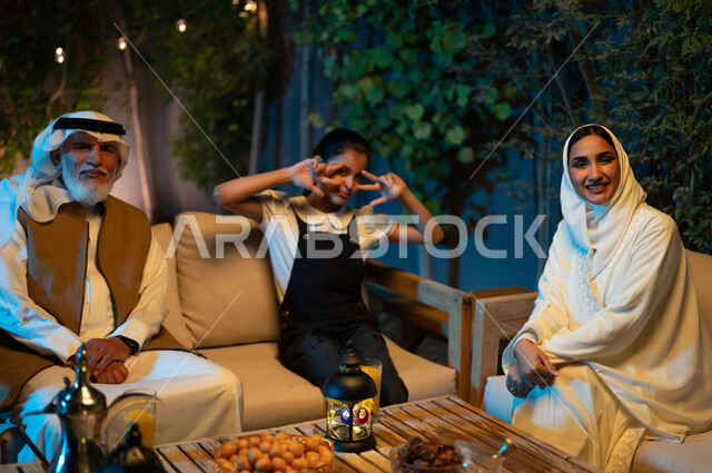 قضاء أوقات ممتعة في جلسة خارجية في احدى الشاليهات، أسرة عربية خليجية سعودية تنظر إلى الكاميرا بإيماءات السرور، المناسبات والأعياد الاسلامية، تبادل الأحاديث والتسامر بين الأفراد، أجواء عائلية سعيدة في شهر رمضان المبارك، فتاة ترفع يديها بتعابير الفرح