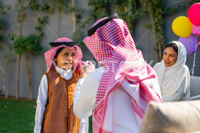 مفهوم الأناقة والاهتمام بالمظهر الخارجي، ارتداء الأزياء التقليدية في المناسبات والأعياد الإسلاميه، صورة مقربة من الخلف لرجل عربي سعودي خليجي يرتدي الزي التقليدي يقوم بتعديل شماغ ابنه, قضاء وقت ممتع في أيام العيد مع العائلة في السعوديه، إيماءات وتعابير السعادة والسرور