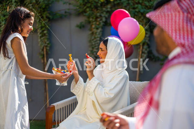 فرحة و بهجة الأطفال في العيد السعيد، فتاة عربية خليجية سعودية ترتدي فستان أبيض تقوم بتقديم قطع السكاكر, عادات العيد في المجتمع السعودي الخليجي، أعياد ومناسبات إسلامية سعيدة, الاحتفال في الهواء الطلق في إحدى الشاليهات والمنتجعات السياحية