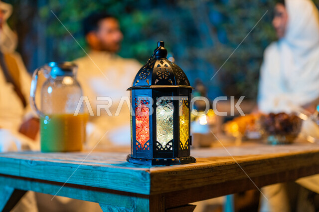 ديكورات وزينة المناسبات والأعياد الاسلامية، تبادل الأحاديث والتسامر بين الأفراد، صورة مقربة لفانوس معدني مضيء على طاولة خشبية، أسرة عربية خليجية سعودية تقضي أوقات ممتعة في جلسة خارجية في احدى الشاليهات، أجواء عائلية سعيدة في شهر رمضان المبارك