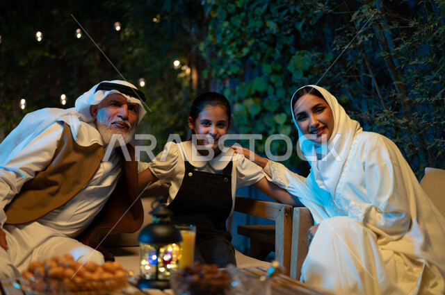 النظر إلى الكاميرا لالتقاط الصور التذكارية، ديكورات وزينة المناسبات والأعياد الاسلامية، أسرة عربية خليجية سعودية تقضي أوقات ممتعة في جلسة خارجية في احدى الشاليهات، أجواء عائلية سعيدة في شهر رمضان المبارك، فانوس معدني مضيء على طاولة خشبية