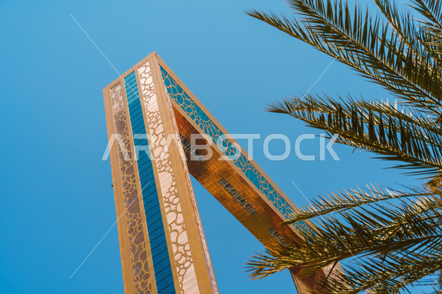 الفن الهنديسي المعماري لبرواز إمارة، النمو والتطور العمراني في دولة الإمارات العربية المتحدة، مبنى ذهبي متحد، ومجسم شخصي زجاجي، اشغال شجرة النخيل الخضراء والنباتات في مدن سياحية واضحة النهار، معالم واماكن سياحية مشهورة في دبي