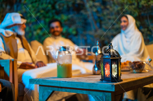 ديكورات وزينة المناسبات والأعياد الاسلامية، تبادل الأحاديث والتسامر بين الأفراد، أسرة عربية خليجية سعودية تقضي أوقات ممتعة في جلسة خارجية في احدى الشاليهات، أجواء عائلية سعيدة في شهر رمضان المبارك، فانوس معدني مضيء على طاولة خشبية