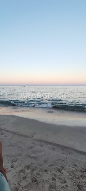 مشهد غروب الشمس في سماء دولة سلطنة عمان, مناظر طبيعية على ساحل البحر الأحمر، الاستمتاع بمنظر المياه في النهار على شاطئ البستان الرملي في مدينة مسقط, مناطق سياحية للرحلات والنزهات العائلية في العطلة الصيفية