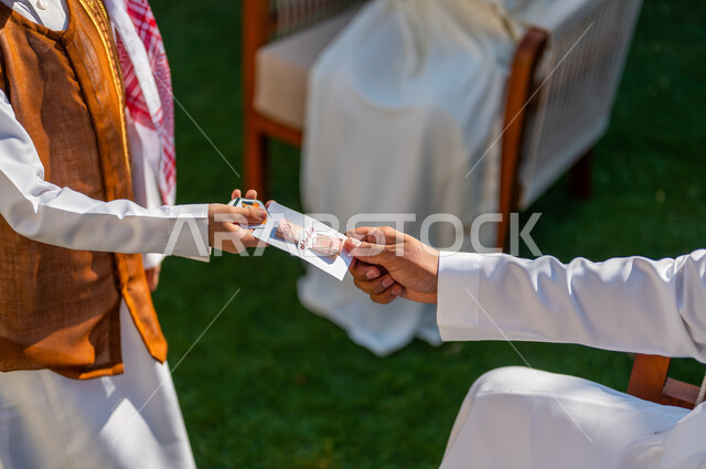 إدخال الفرحة والبهجة لقلوب الأولاد، طقوس العادات والتقاليد العربية في المناسبات والأعياد الاسلامية، صورة مقربة من الجانب ليد فتى عربي سعودي خليجي يرتدي الملابس الجديدة ويأخذ العيدية من والده، قضاء وقت ممتع في أيام العيد في السعوديه