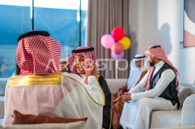 أعياد ومناسبات دينية، صورة مقربة من الخلف لرجل يرتدي الزي التقليدي، أسرة عربيه خليجية سعودية تجلس في غرفة المعيشة تقوم بالاحتفال بالعيد، قضاء اوقات ممتعة مع الابناء