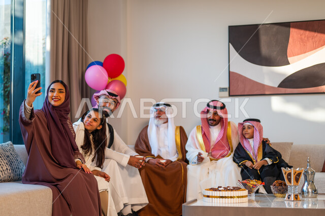 Using modern technology to preserve special moments, wearing traditional clothes on holidays and religious occasions, a Saudi Gulf Arab family meeting in the living room, using balloons for decoration.