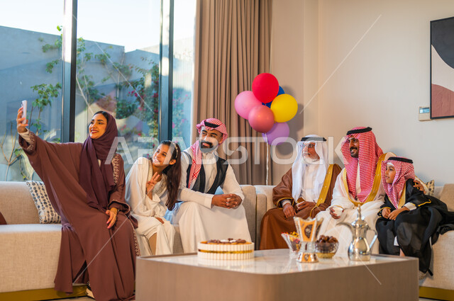 التقاط الصور التذكارية، ارتداء الملابس التقليدية في الأعياد والمناسبات الدينية، أسرة عربيه خليجية سعودية تجتمع في غرفة الجلوس، ايماءات البهجة والسرور، استخدام البوالين للزينة