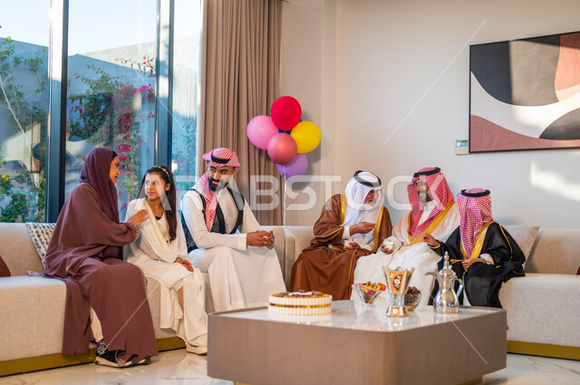 الاحتفال بالأعياد والمناسبات الدينية، مشاركة الأحاديث الممتعة مع العائلة، أسرة عربيه خليجية سعودية تجتمع في غرفة الجلوس، ايماءات البهجة والسرور، استخدام البوالين للزينة