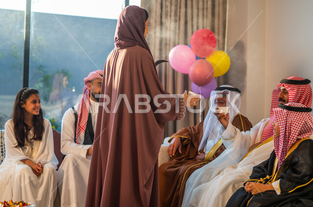 مفهوم الكرم وحسن الضيافة، عادات العيد في المجتمع السعودي، امرأة عربية خليجية سعودية ترتدي العباءة تقوم بتقديم القهوة العربية للضيوف، ايماءات البهجة والسرور، اجتماع الأسرة في غرفة الجلوس