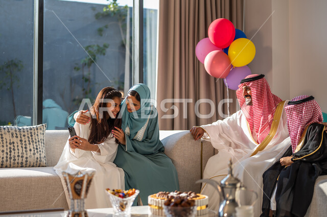 Using balloons for decoration, sharing interesting conversations with the family, a Saudi Gulf Arab family meeting in the living room, celebrating religious holidays and occasions, gestures of joy and pleasure.