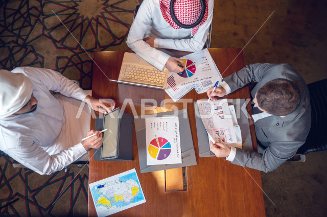 اجتماع اداري مع مجموعة من الأشخاص الخليجيون ، اجتماع رجال اعمال اماراتيون وسعوديون في غرفة الاجتماعات  ، مجموعة من الاوراق المبعثرة على طاولة الاجتماعات ،  ندماج شركة اماراتية و شركة سعودية 