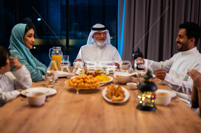 تبادل نظرات المودة بين الزوجين، إيماءات السعادة والسرور، أجواء دينية رمضانية، صورة مقربة لعائلة عربية خليجية سعودية مجتمعة حول مائدة الطعام، سفرة مليئة باصناف من المأكولات الشرقية الشهية، أداء فريضة الصيام