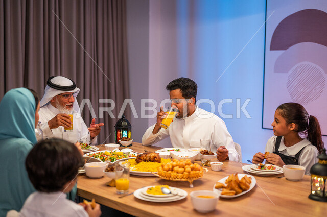 إيماءات التركيز و الانتباه، أجواء دينية رمضانية، صورة مقربة لعائلة عربية خليجية سعودية مجتمعة حول مائدة الطعام، سفرة مليئة باصناف من المأكولات الشرقية الشهية، أداء فريضة الصيام، تبادل الأحاديث بين أفراد الأسرة