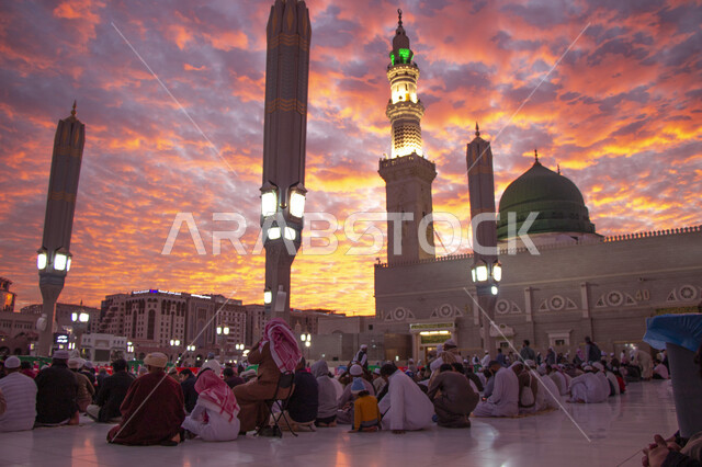 تجمع المسلمون في الساحة الخارجية للحرم النبوي الشريف في المدينة المنورة، معالم دينية مقدسة في المملكة العربية السعودية، اسلاميات وعبادة، منظر السماء المليئة بالغيوم والسحب وقت غروب الشمس، الطاعة والتقرب إلى الله, الفن الهندسي المعماري الاسلامي لمسجد رسول الله
