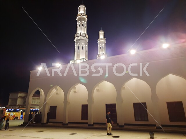 الزوار والمصلين في الفناء الخارجي للجامع، قبب ومآذن مسجد العريش المضيئة في بدر قرب المدينة المنورة ليلا، الفن الهندسي المعماري المتميز والديكورات الاسلامية على الطراز الحديث، العبادة والتقرب إلى الله، معالم و أماكن دينية مقدسة في المملكة العربية السعودية