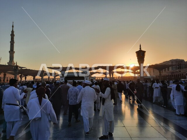 تجمع المسلمون في المجمع الخارجي للمسجد النبوي في المدينة المنورة في وقت الغروب، أماكن و معالم دينية مقدسة  في المملكة العربية السعودية، المآذن والمظلات الالكترونية، الفن الهندسي المعماري للجوامع على الطراز الإسلامي