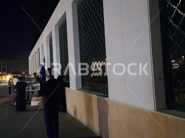 Historical, popular heritage areas, the headquarters of the martyrs of the Battle of Badr in Medina at night, visitors gathered in front of the iron windows overlooking the cemetery, famous Islamic religious places and landmarks in the Kingdom of Saudi Arabia
