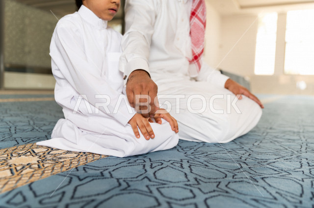 Teaching the performance of the obligatory prayer for a child inside the mosque, a Saudi man prays in the chapel next to his adult son, reverence in the prayer, performing the obligatory prayer in the mosque, worship and drawing closer to God, teaching pr